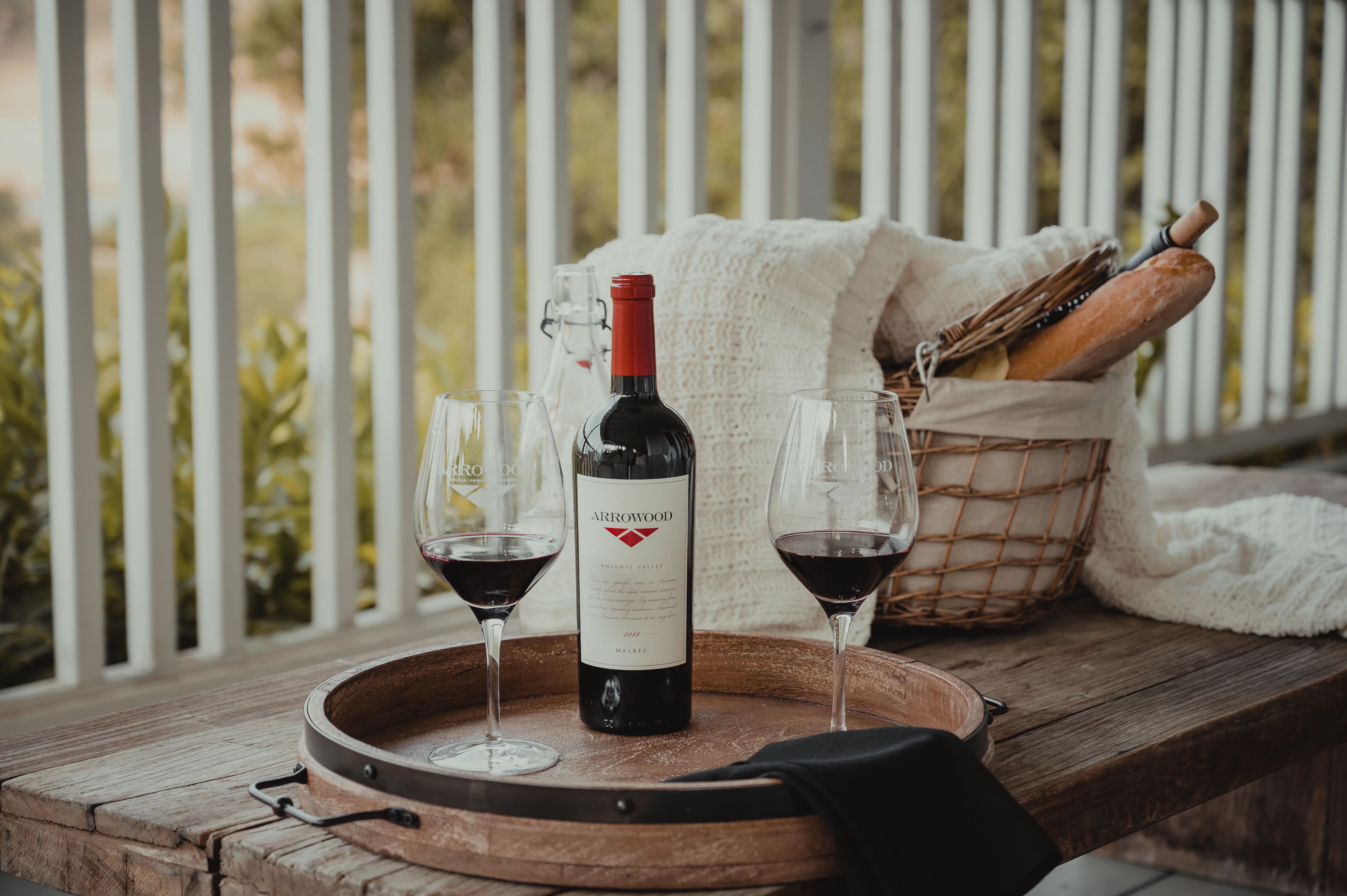 A table with a bottle of wine and two glasses on a porch